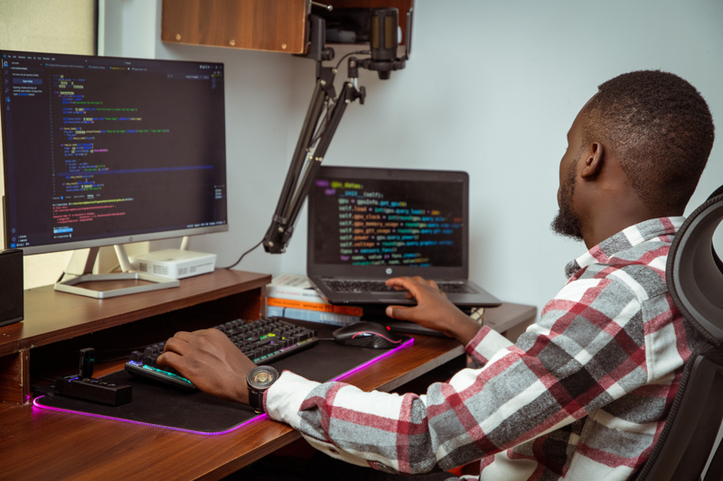 A developer's full workspace with monitors, notebooks, and coffee — ideas on paper, proof in code